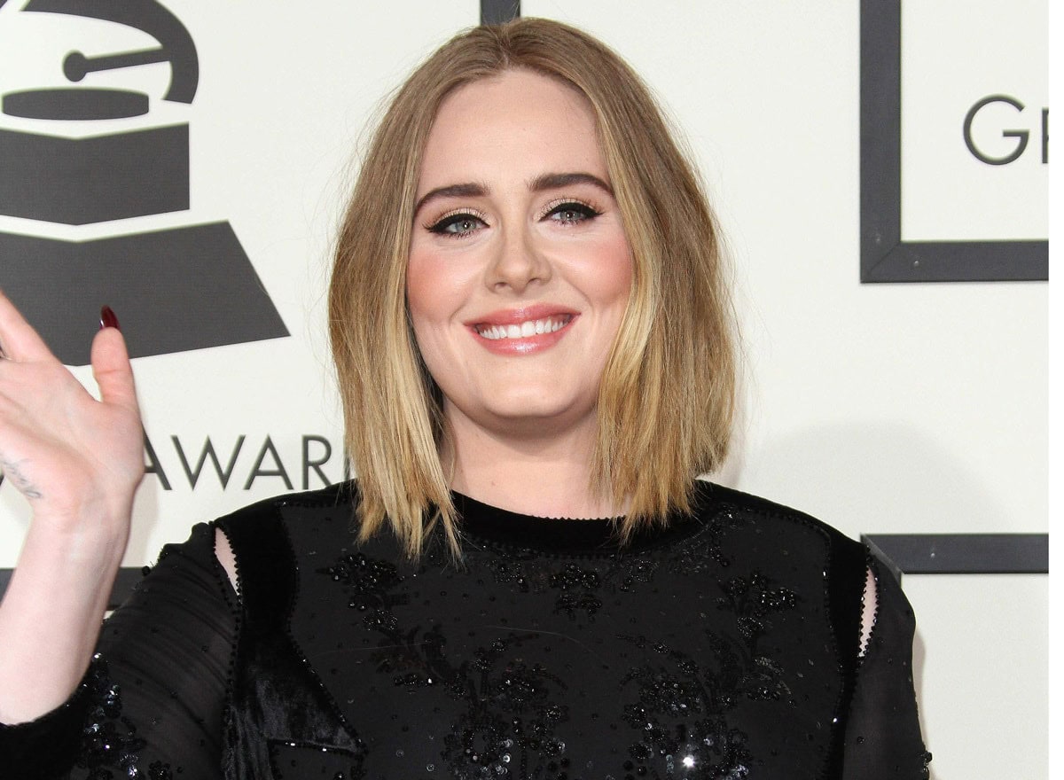Ein künstlerisches Porträtfoto der Sängerin Adele in einem dramatischen, schulterfreien schwarzen Oberteil mit ihrem typischen Eyeliner-Look.