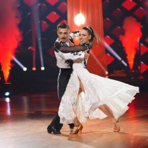 Bibi Heinicke tanzt bei Let's Dance mit ihrem Partner einen Standardtanz in fließendem weißen Kleid vor roter Bühnenbeleuchtung