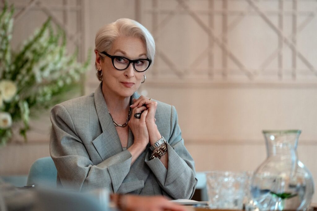 Meryl Streep als Miranda Priestly mit weißem Haar, Cat-Eye-Brille und elegantem Hosenanzug in nachdenklicher Pose