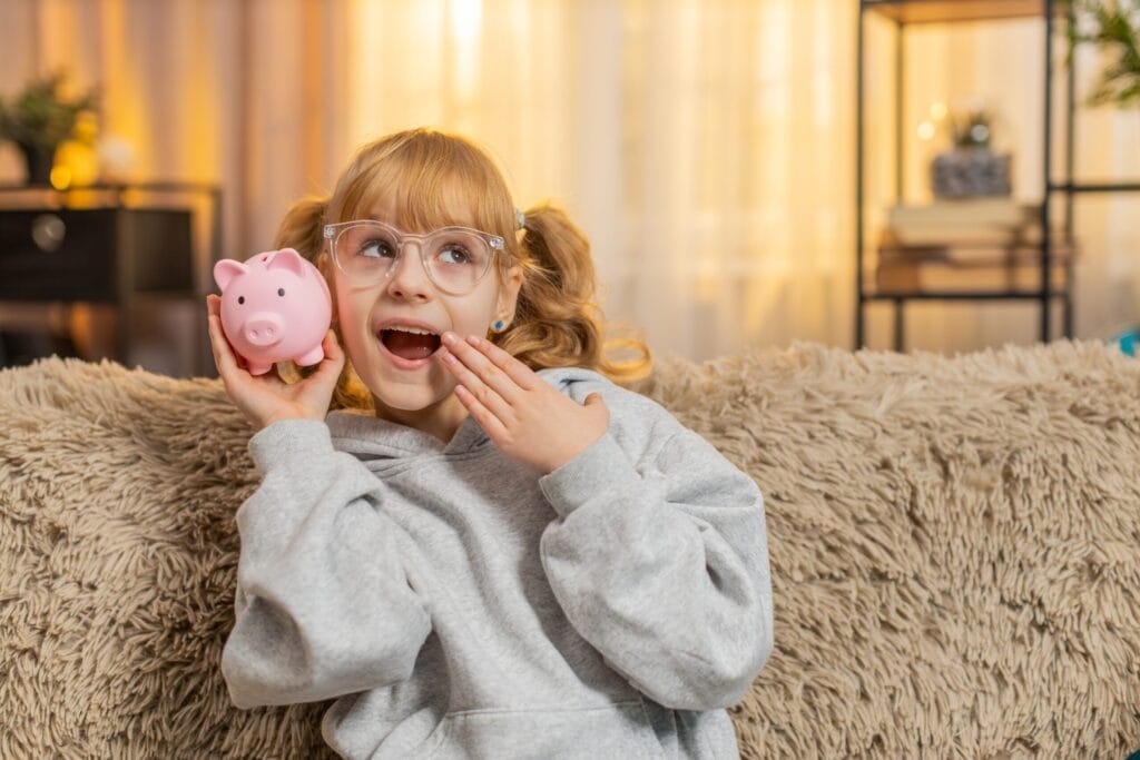 Kind hält fröhlich ein Sparschwein mit erstem Taschengeld