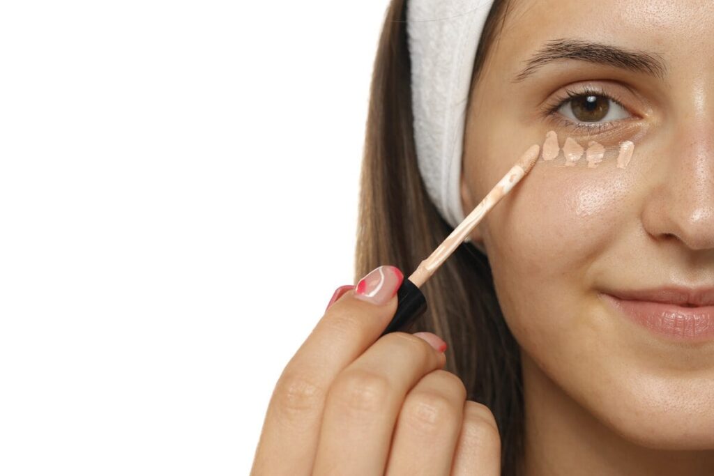 Frau tupft mit dem Pinsel Concealer unter das Auge, um Augenringe abzudecken