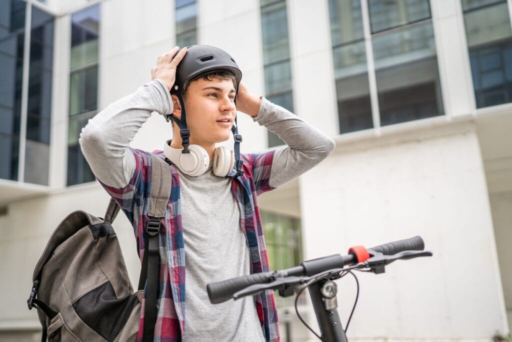 Junger Mann setzt vor der Fahrt mit dem E-Scooter seinen Helm auf