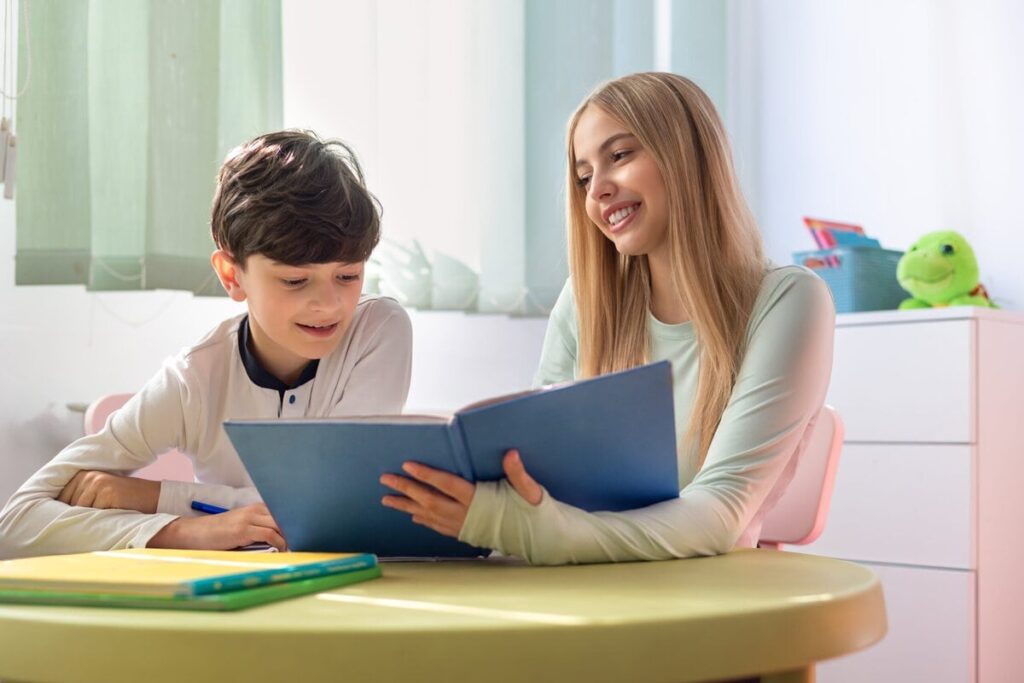 Teenagerin gibt mit 14 einem jüngeren Kind Nachhilfe am Schreibtisch