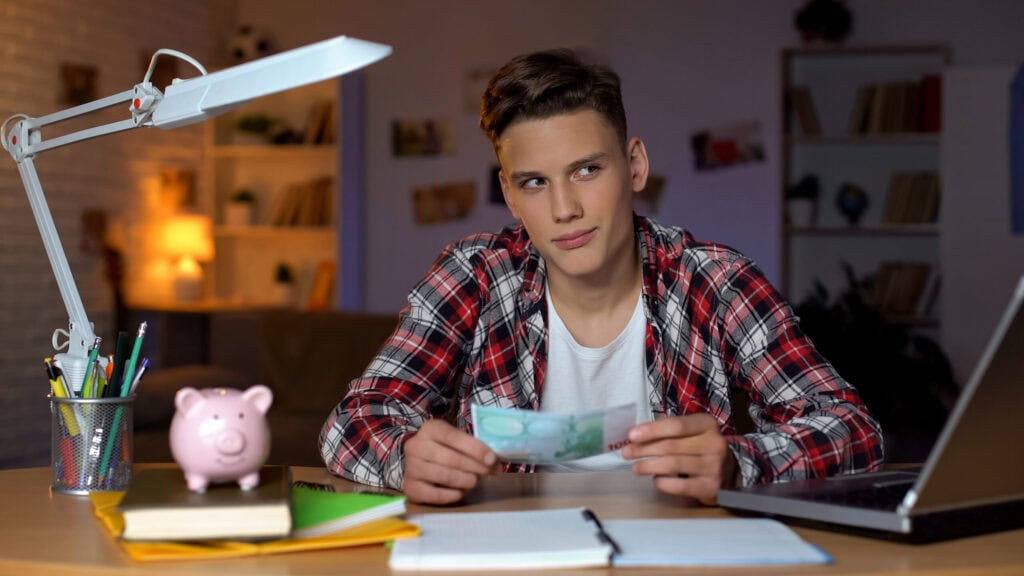 Taschengeld mit 14: Jugendlicher mit Euro-Schein am Schreibtisch