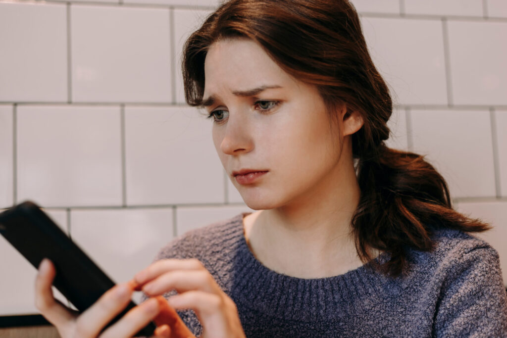 Junge Frau wartet enttäuscht aufs Handy, ein Anzeichen für eine Situationship
