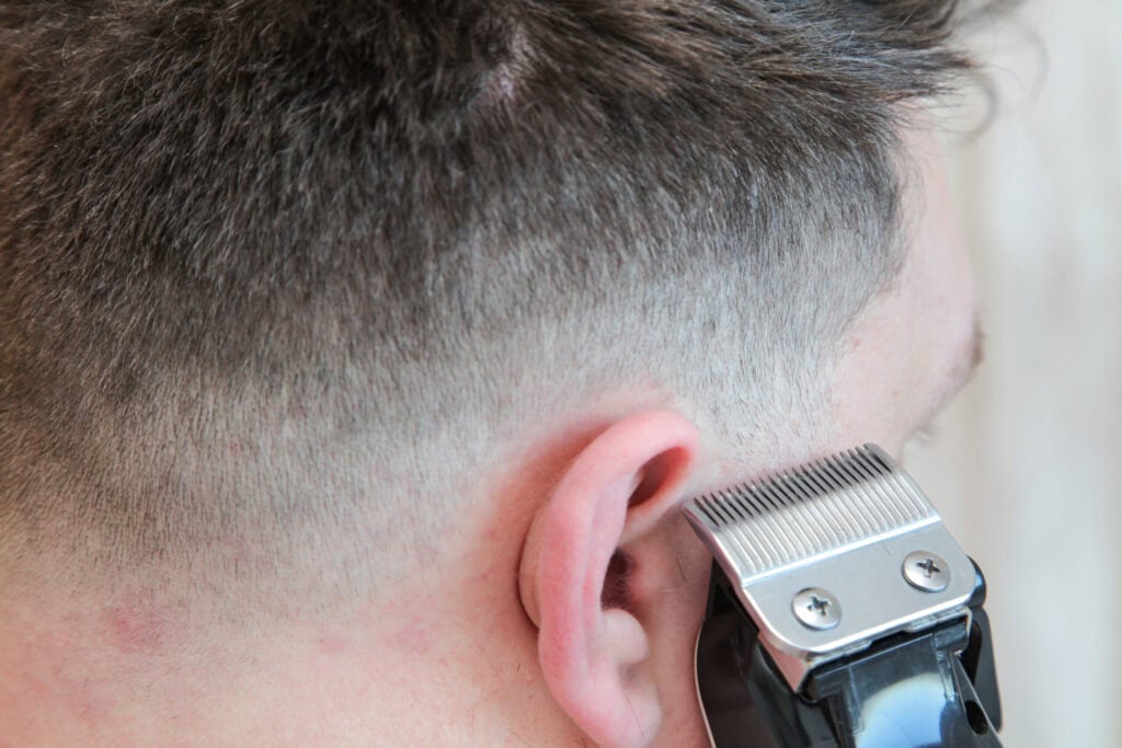 Barber schneidet den Fade-Übergang am Ohr mit der Haarschneidemaschine nach