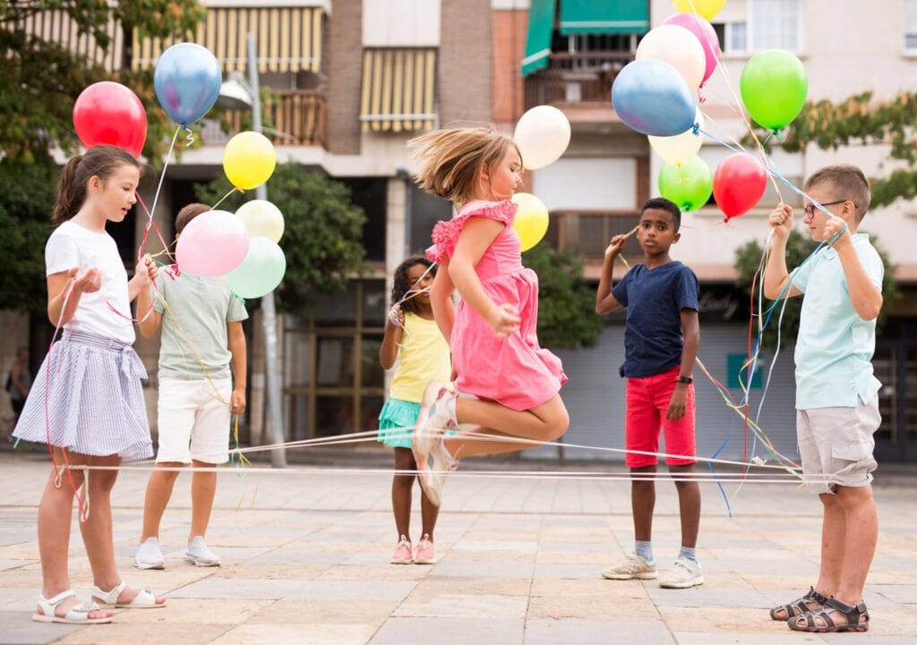 Kinder spielen draußen auf der Straße mit Gummitwist und bunten Luftballons