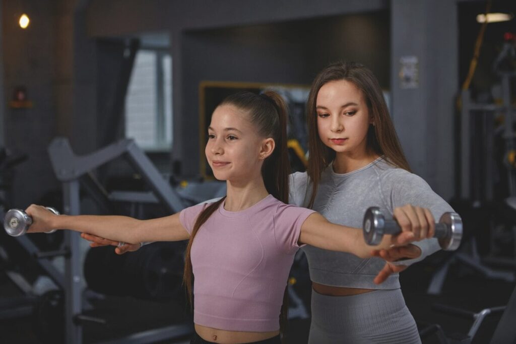 Trainerin korrigiert die Technik einer Jugendlichen beim Krafttraining mit Kurzhanteln
