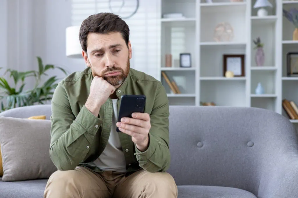 Mann schaut nachdenklich aufs Handy und überlegt, jemanden zu ghosten