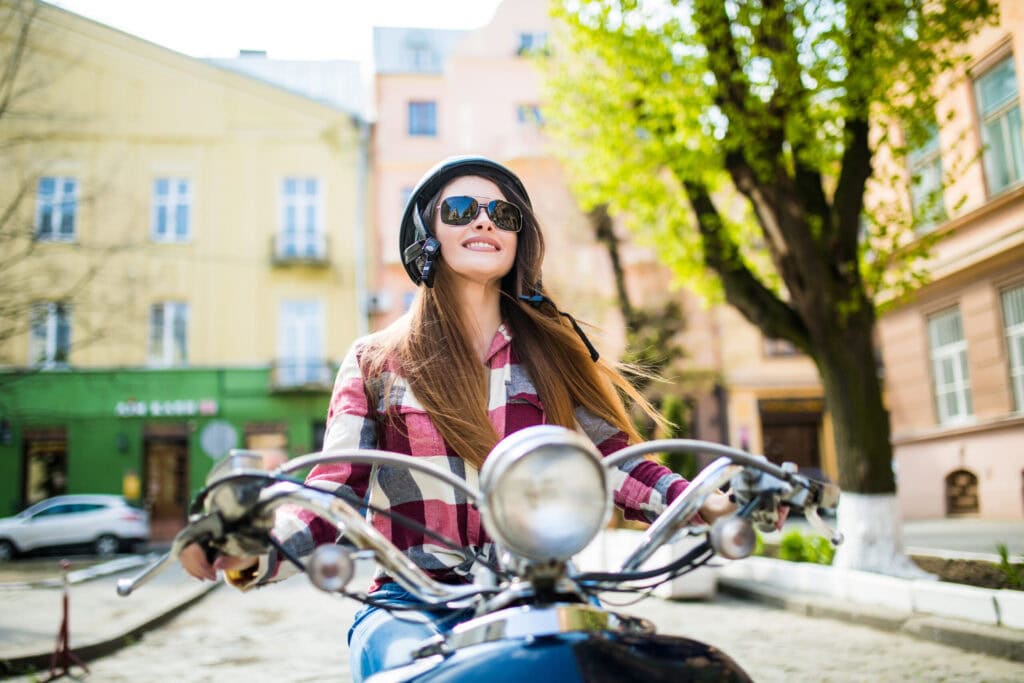 Junge Frau mit Helm fährt mit wehenden Haaren auf dem Roller durch die Stadt